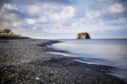 Relax on the black sand beach of Stromboli and enjoy views of the small promontory of Strombolicchio