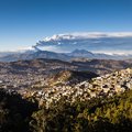 Quito in the foreground with an erupting Cotopaxi volcano in the distance