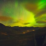 A car pulls over to witness green Northern Lights over an Icelandic setting