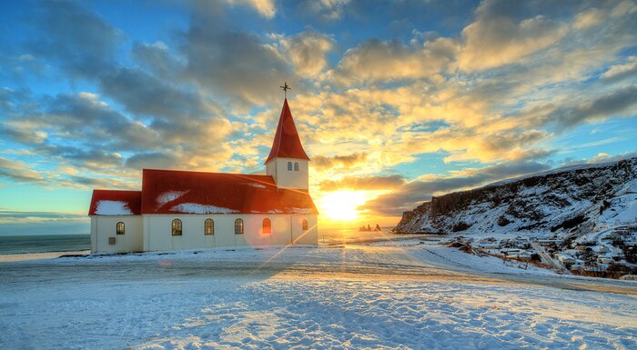 Snowfall over the red-roofed church in Vík