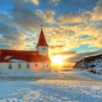 Snowfall over the red-roofed church in Vík