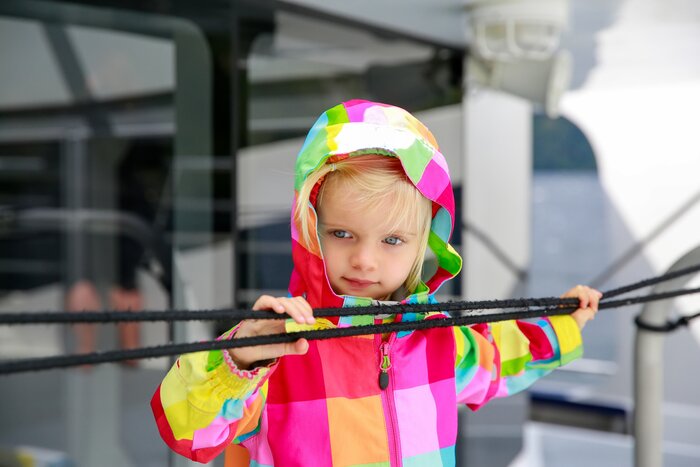 Adorable kid in colorful coat looking at water from the touring boat, Te Anau, New ZealandFamily frolicking in the sea near Auckland