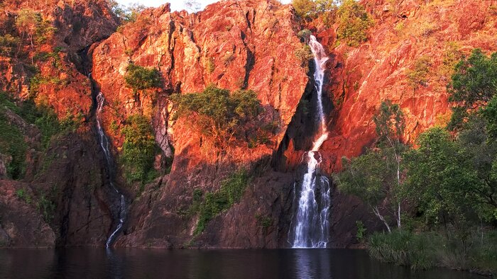 The setting sun turns the cliffs at Wangi Falls in Litchfield National Park a brilliant red
