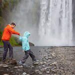 Father and son hopping on rocks and enjoying Skógafoss waterfall in Iceland