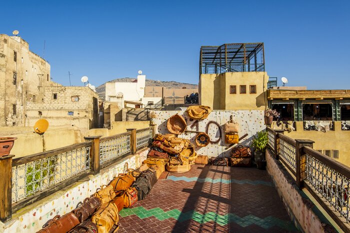 Variety of leather bags and poufs exposed for sale on a terrace with a tannery view in Fes, Morocco