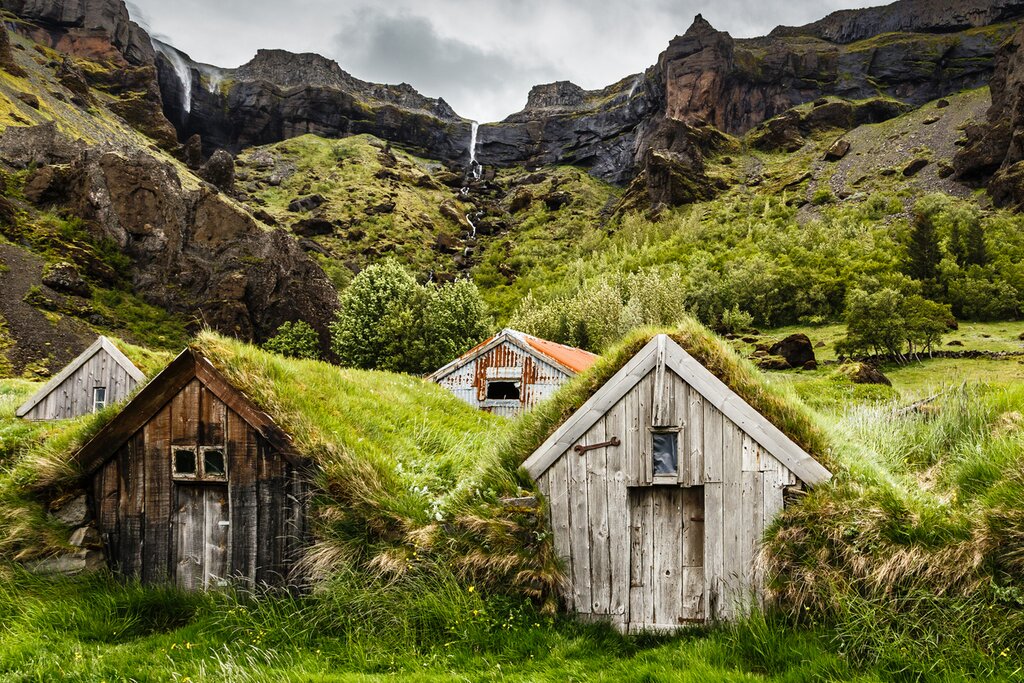 Icelandic turf houses and rocky canyon with waterfall in the background near Kalfafell vilage, South Iceland