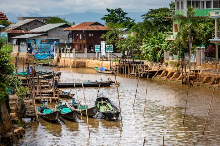 Canton de Nyaungshwe, Shan / Myanmar. July 31, 2019: Inle Boat Station in Inle Nyaung Shwe Canal. A series of fishing boats along the river generated by Inle Lake. Homes in the background.